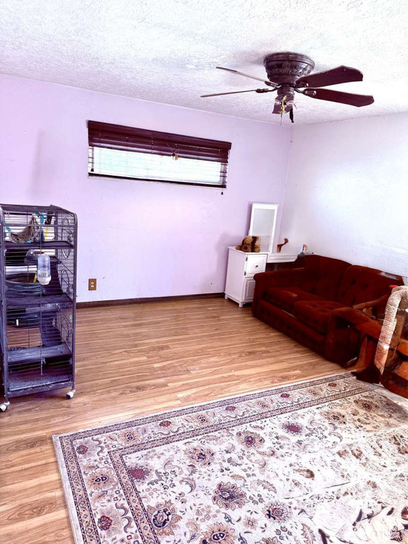 Sitting room featuring a ceiling fan, light wood-style floors, a textured ceiling, and baseboards