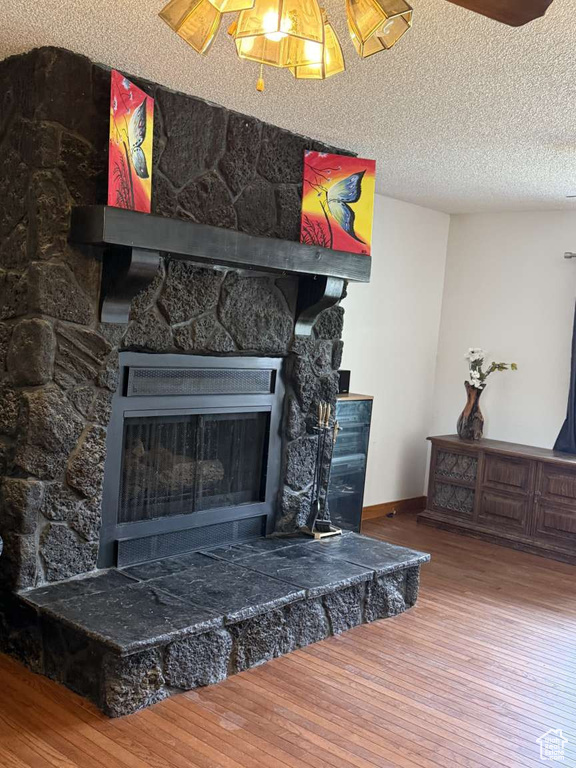 Detailed view of wood finished floors, a stone fireplace, a textured ceiling, and baseboards