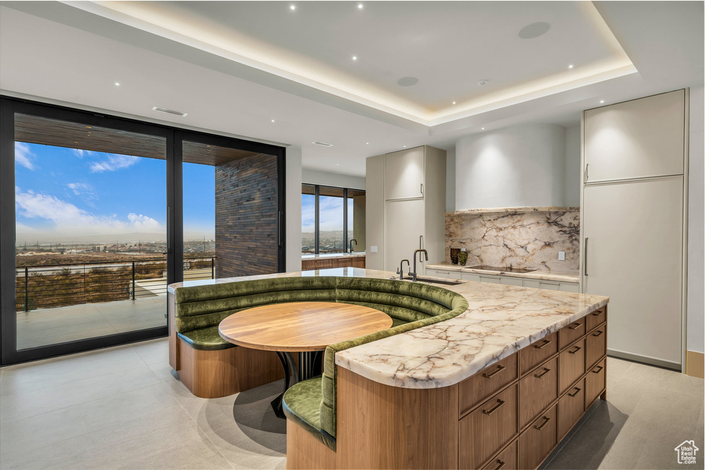 Kitchen featuring modern cabinets, a kitchen island with sink, tasteful backsplash, expansive windows, and a raised ceiling