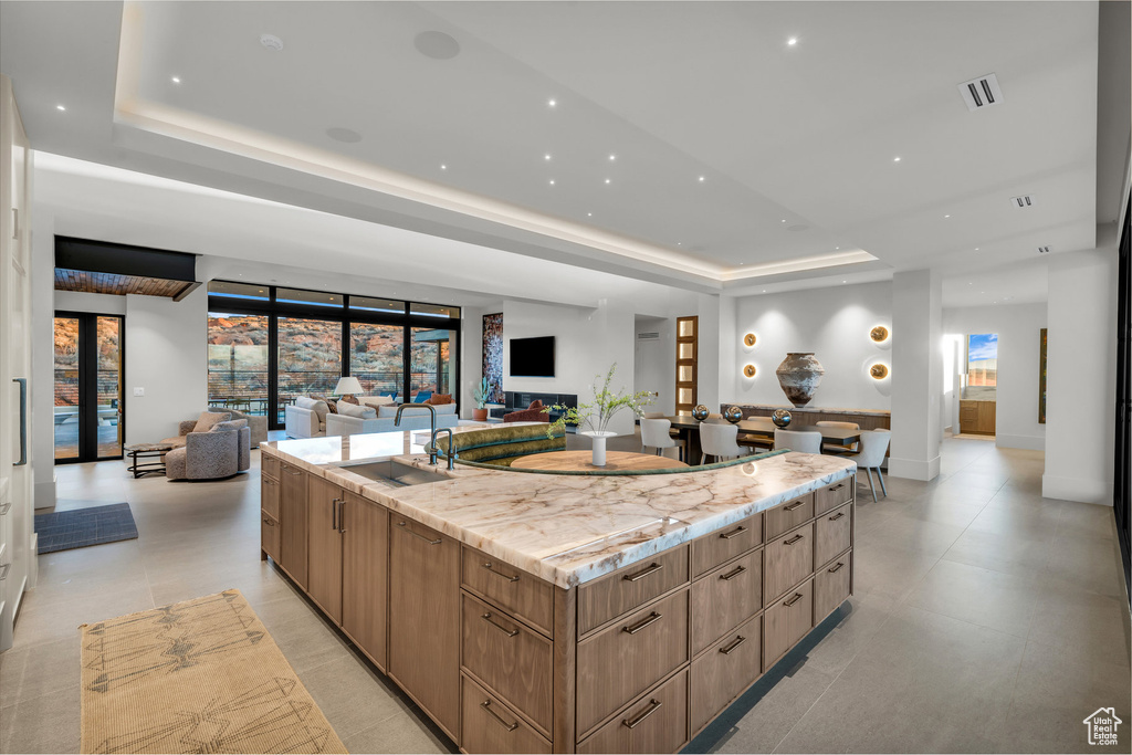 Kitchen with a tray ceiling, modern cabinets, open floor plan, a spacious island, and light stone countertops