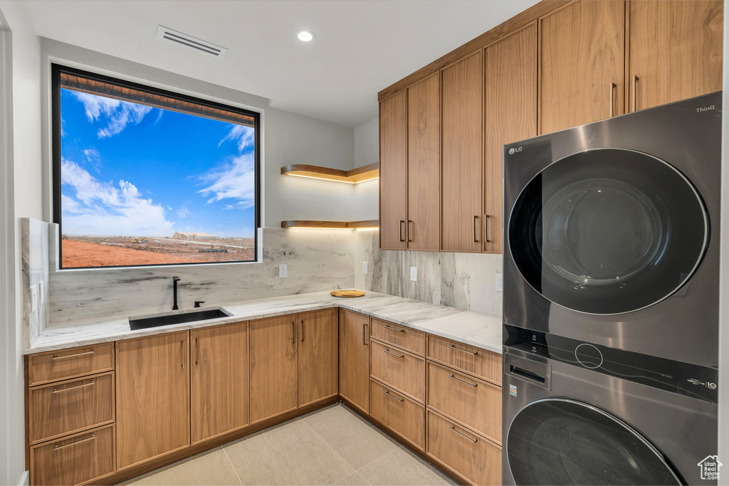 Laundry area featuring estacked washer and dryer, cabinet space, recessed lighting, and light tile patterned floors