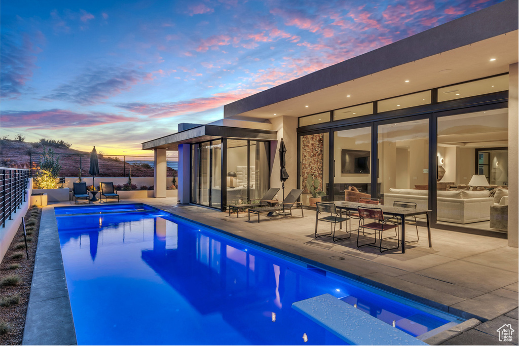 Pool at dusk with a patio, an outdoor hangout area, and exterior kitchen