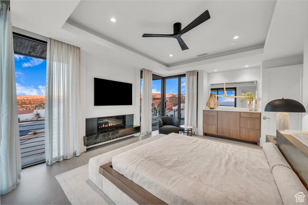 Bedroom featuring a raised ceiling, access to outside, a glass covered fireplace, recessed lighting, and a ceiling fan