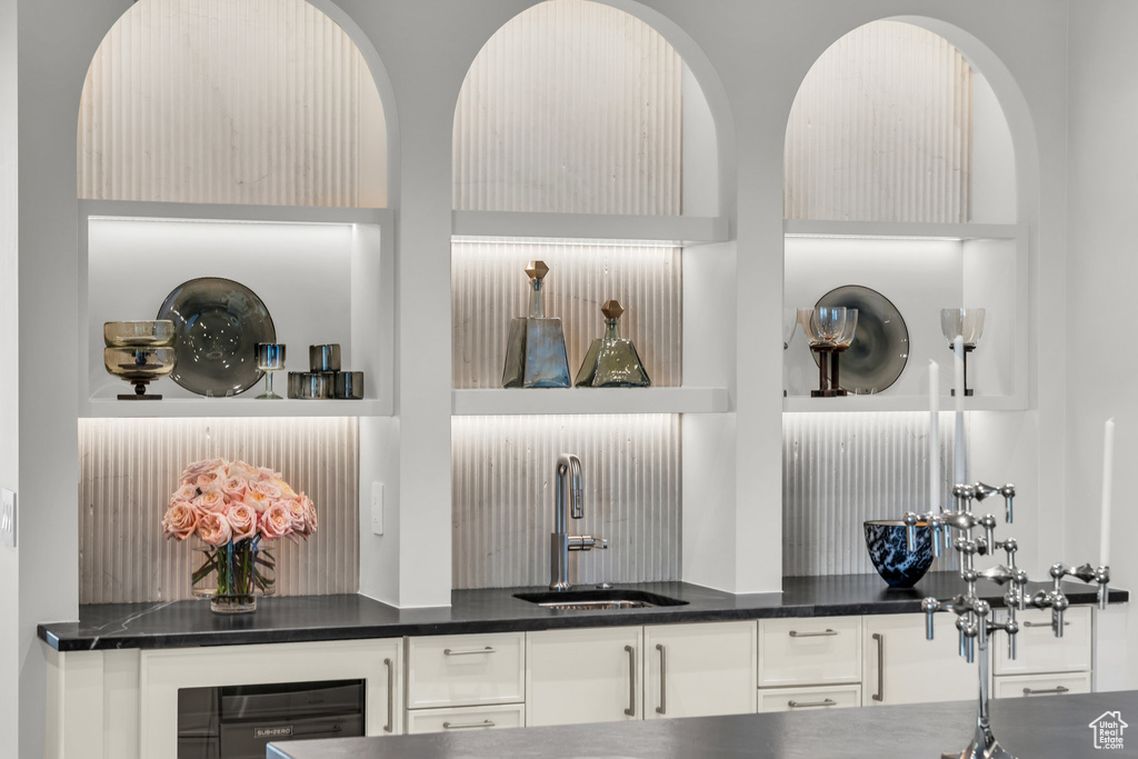 Detailed view of bar with sink, dark countertops, white cabinetry, and beverage cooler