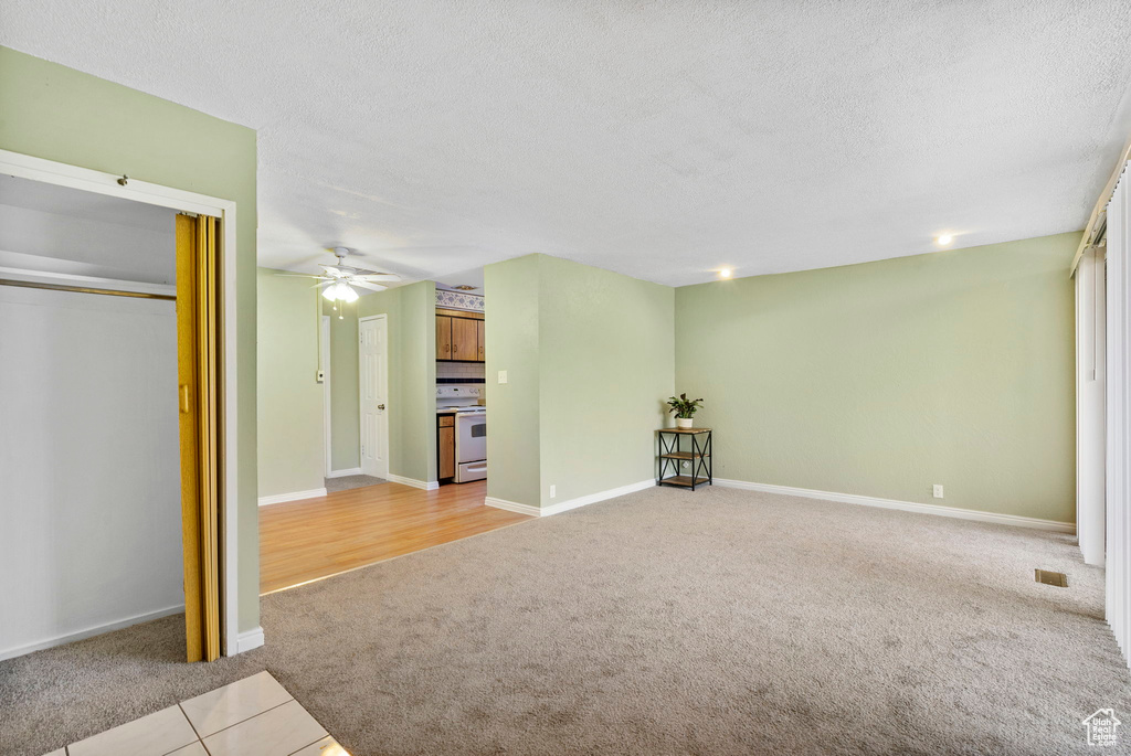 Unfurnished living room with ceiling fan, light colored carpet, and a textured ceiling