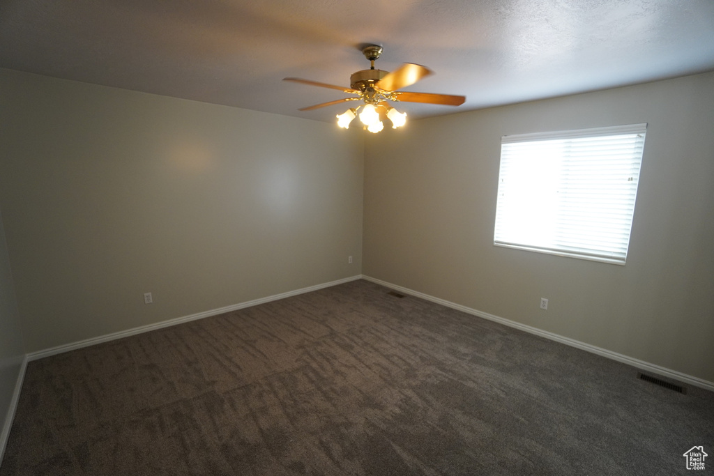 Unfurnished room featuring ceiling fan and dark colored carpet