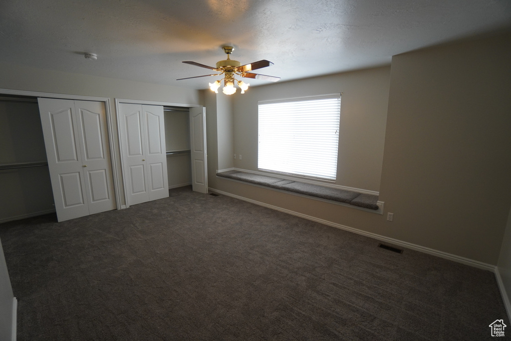 Unfurnished bedroom with multiple closets, ceiling fan, and dark carpet