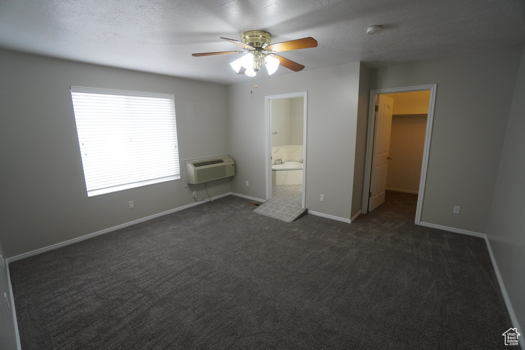 Unfurnished bedroom featuring a spacious closet, an AC wall unit, a textured ceiling, and dark colored carpet