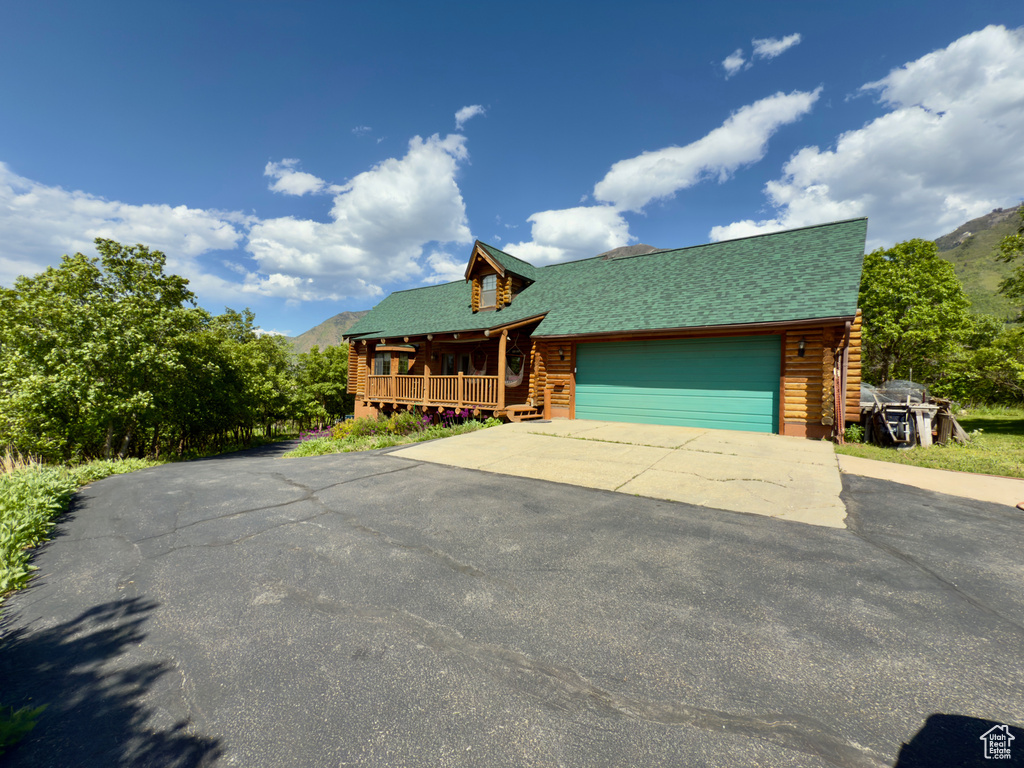 Cabin featuring log exterior, covered porch, asphalt driveway, a mountain view, and a garage