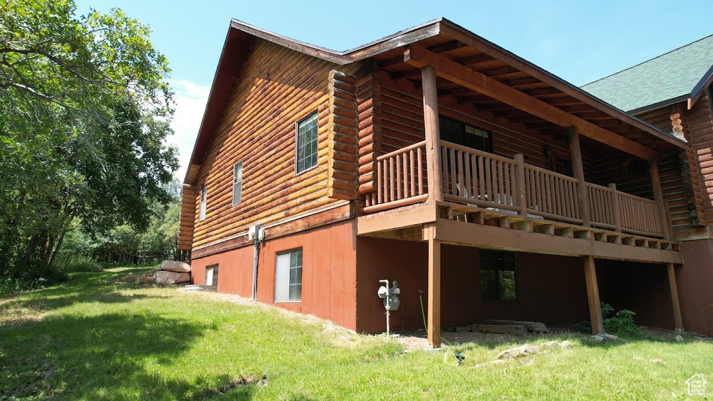 View of side of property with a yard, log siding, a deck, and roof with shingles