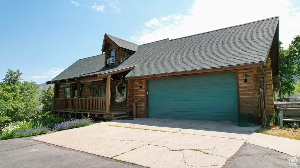Log cabin featuring a porch, a shingled roof, log siding, an attached garage, and concrete driveway