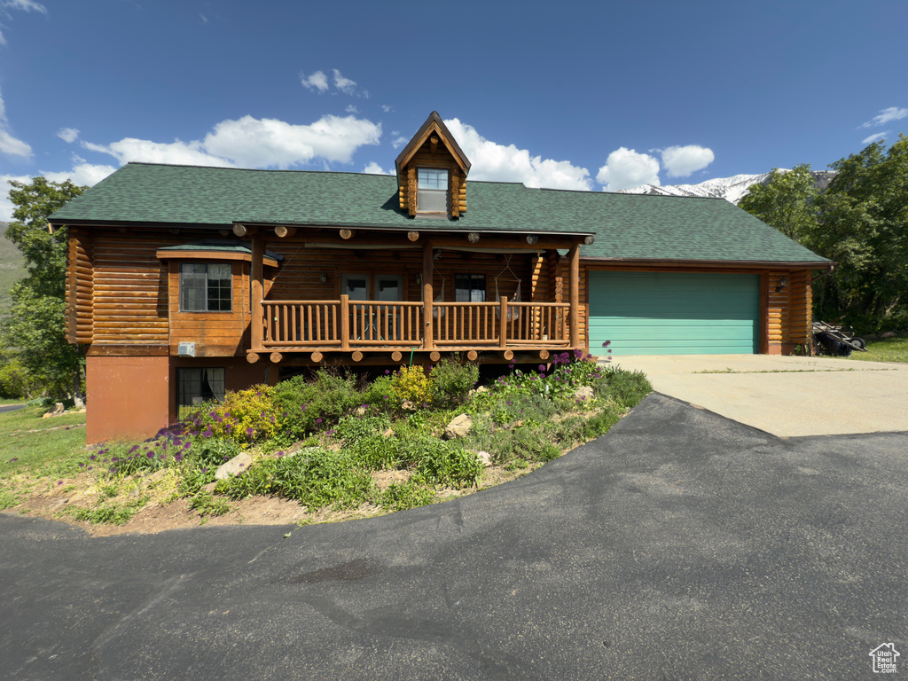 Cabin with log siding, driveway, a garage, and covered porch
