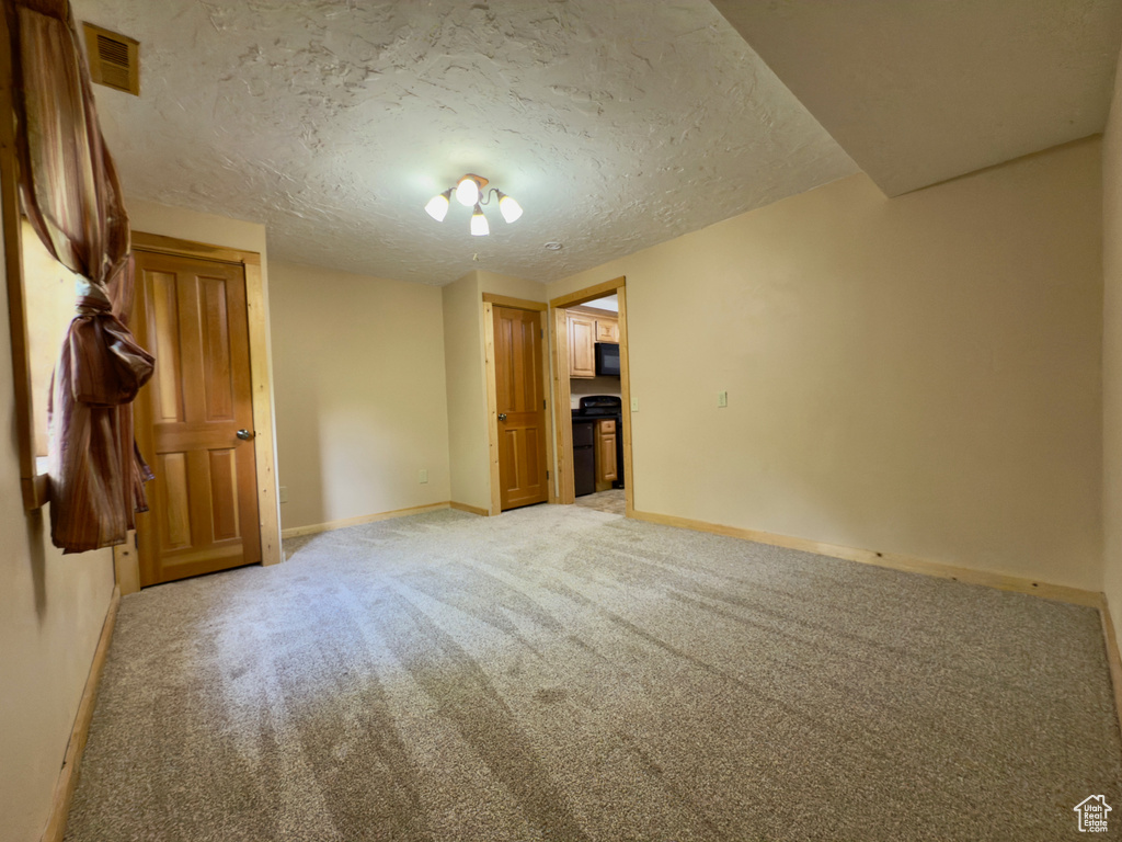 Empty room with light colored carpet, baseboards, and a textured ceiling