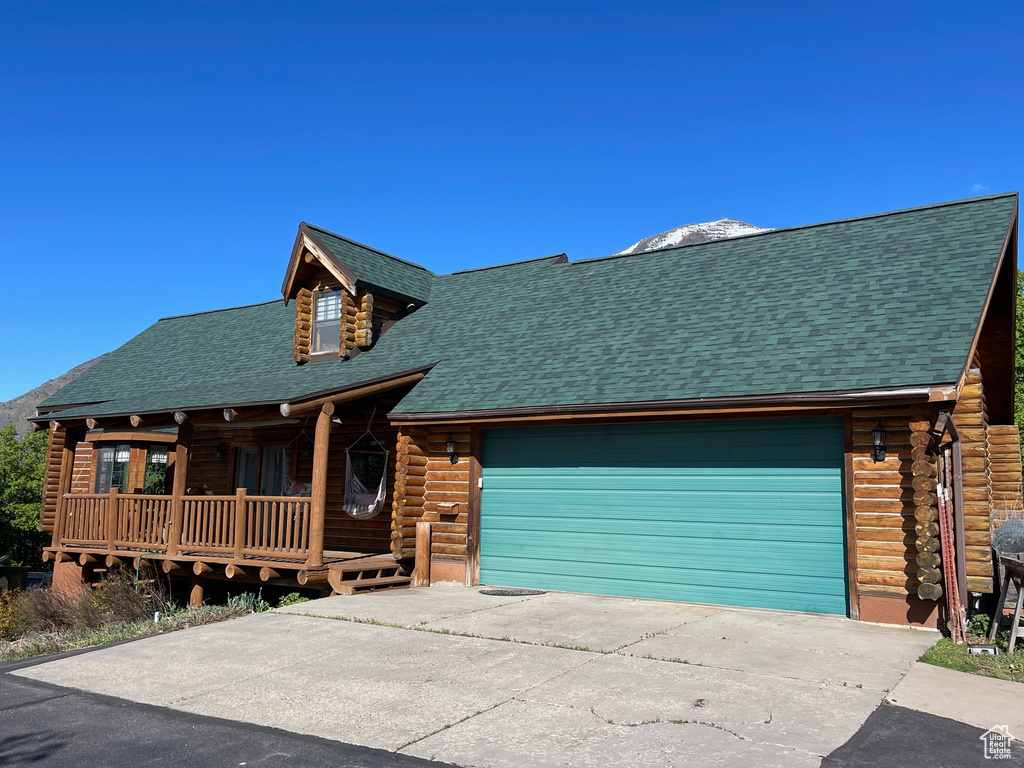 Log home featuring covered porch, log siding, a garage, concrete driveway, and a shingled roof