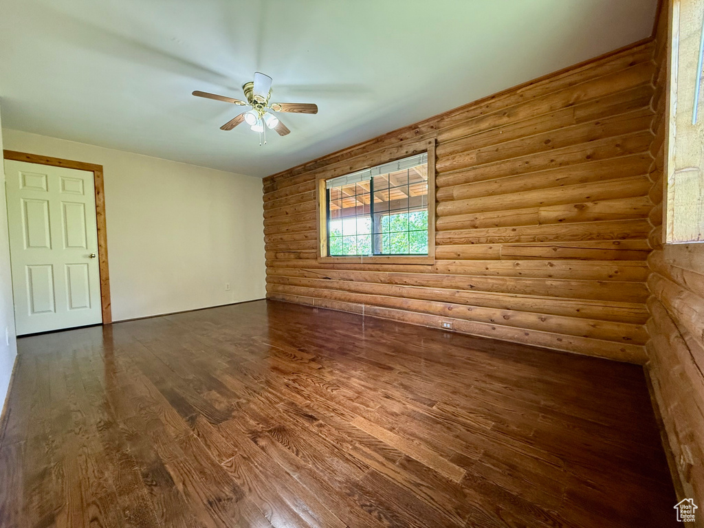 Empty room featuring a ceiling fan, dark wood-type flooring, and log walls