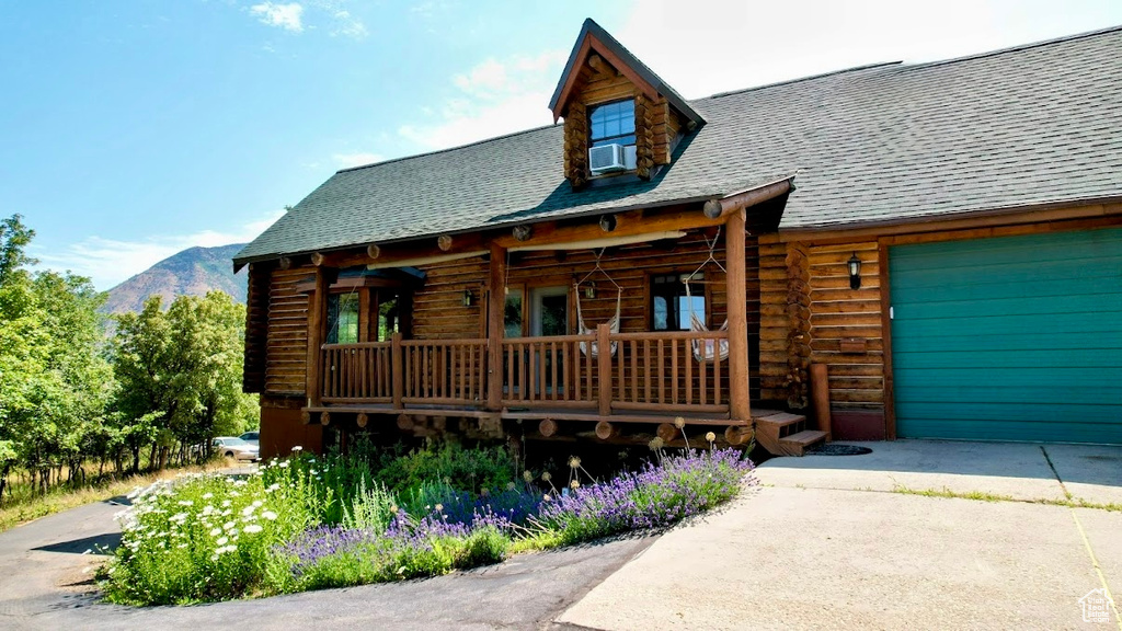 Cabin with log exterior, a shingled roof, a mountain view, driveway, and an attached garage