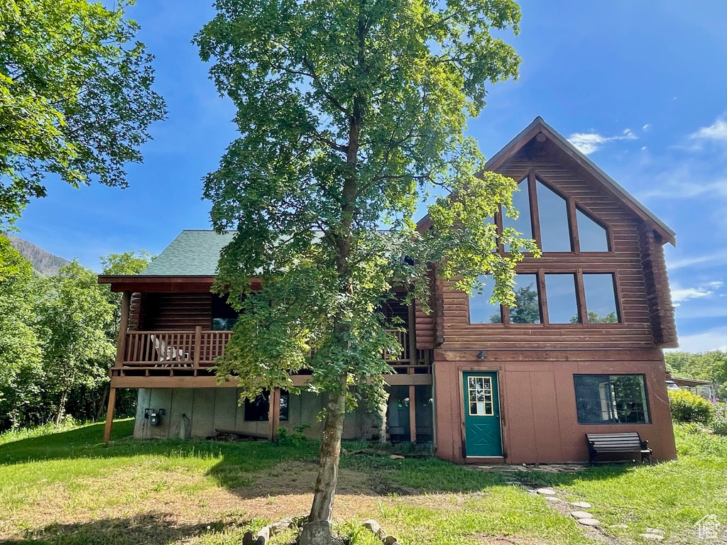 Back of house featuring log exterior, a lawn, and a wooden deck