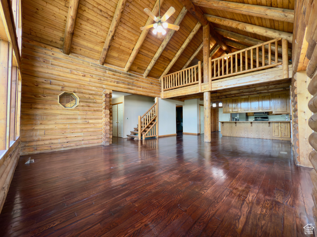 Unfurnished living room featuring high vaulted ceiling, dark wood-type flooring, stairs, ceiling fan, and wood ceiling with exposed beams