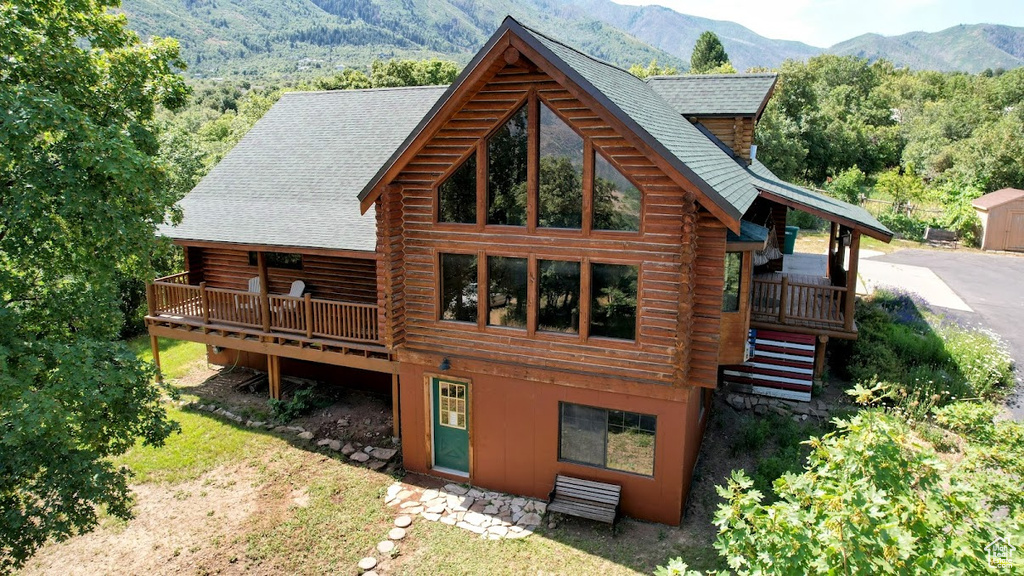 Rear view of house featuring log exterior, a deck with mountain view, and a shingled roof