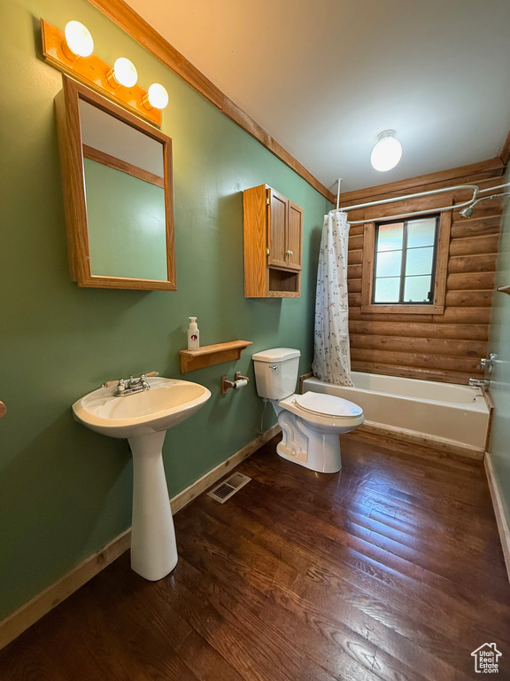 Bathroom with toilet, baseboards, shower / tub combo, wood finished floors, and log walls