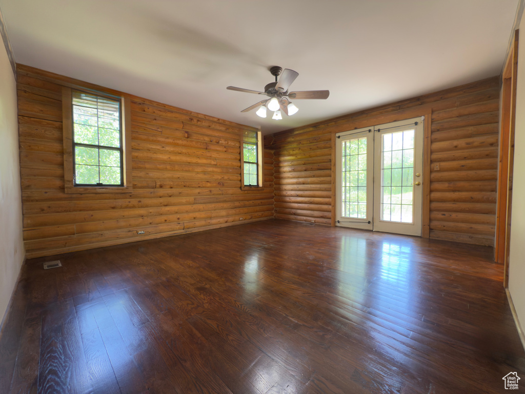 Unfurnished room with ceiling fan, dark wood finished floors, plenty of natural light, and log walls