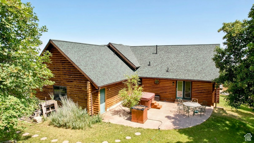 Back of property with a hot tub, a patio, log exterior, and a lawn