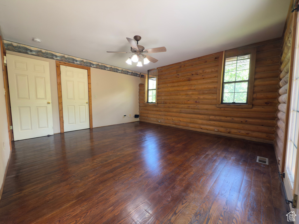 Empty room with dark wood-type flooring, a ceiling fan, rustic walls, and a smoke detector