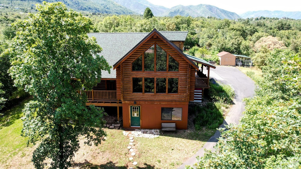 View of front of house with log siding, a forest view, a shingled roof, and a deck with mountain view