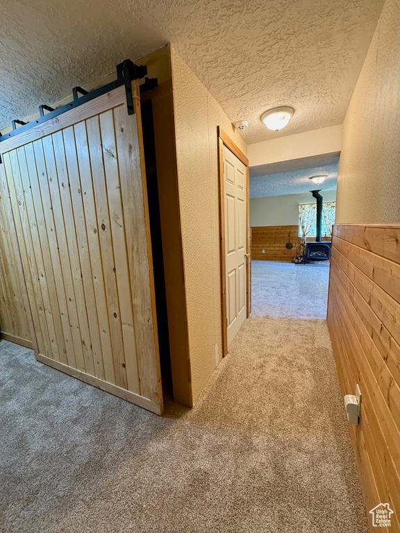 Hallway featuring a textured ceiling, carpet, a wainscoted wall, and wood walls