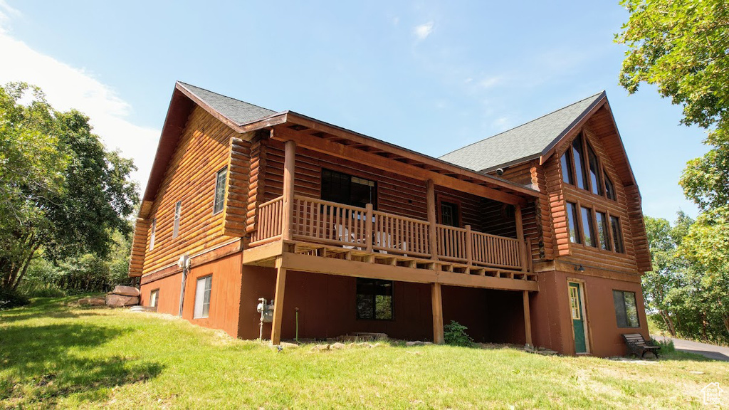 Rear view of house featuring a lawn, roof with shingles, log siding, and a deck