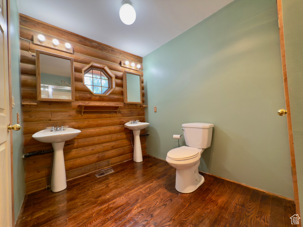 Bathroom featuring log walls, wood finished floors, a sink, and toilet