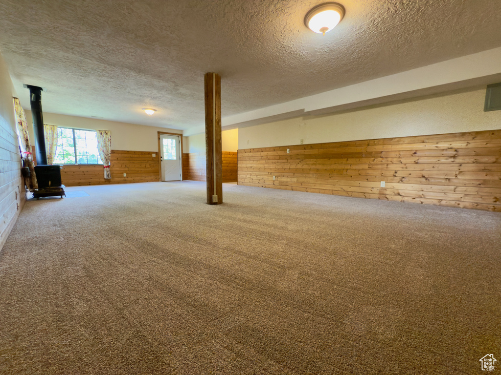 Basement featuring wooden walls, a wood stove, a textured ceiling, a wainscoted wall, and carpet