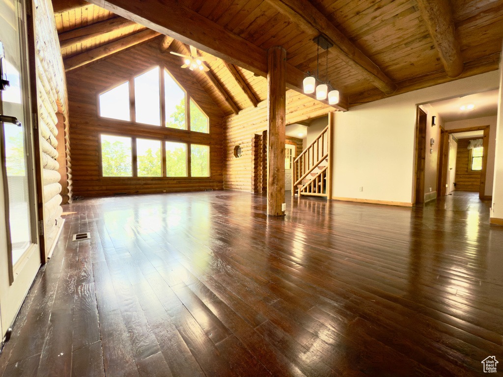 Unfurnished living room with hardwood / wood-style floors, healthy amount of natural light, wooden ceiling with exposed beams, stairway, and high vaulted ceiling