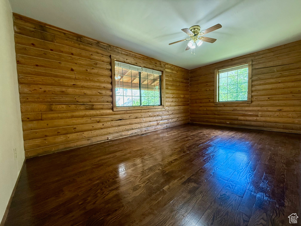 Unfurnished room featuring log walls, dark wood-style flooring, and a ceiling fan