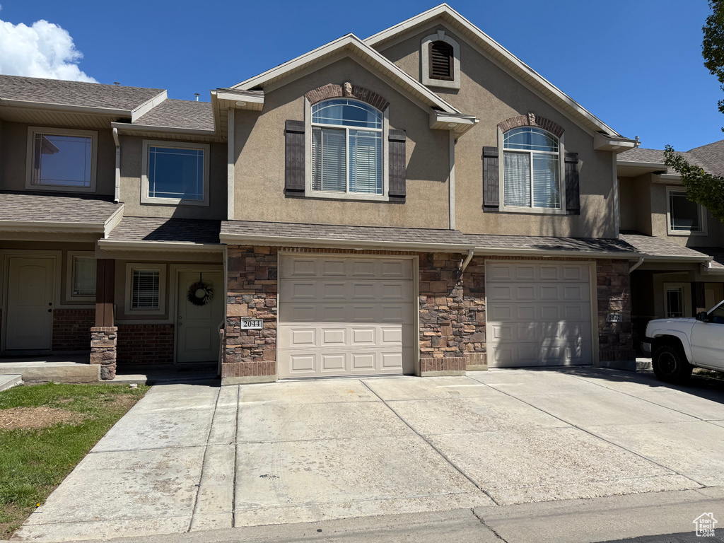 View of property featuring stucco siding, driveway, stone siding, and a garage