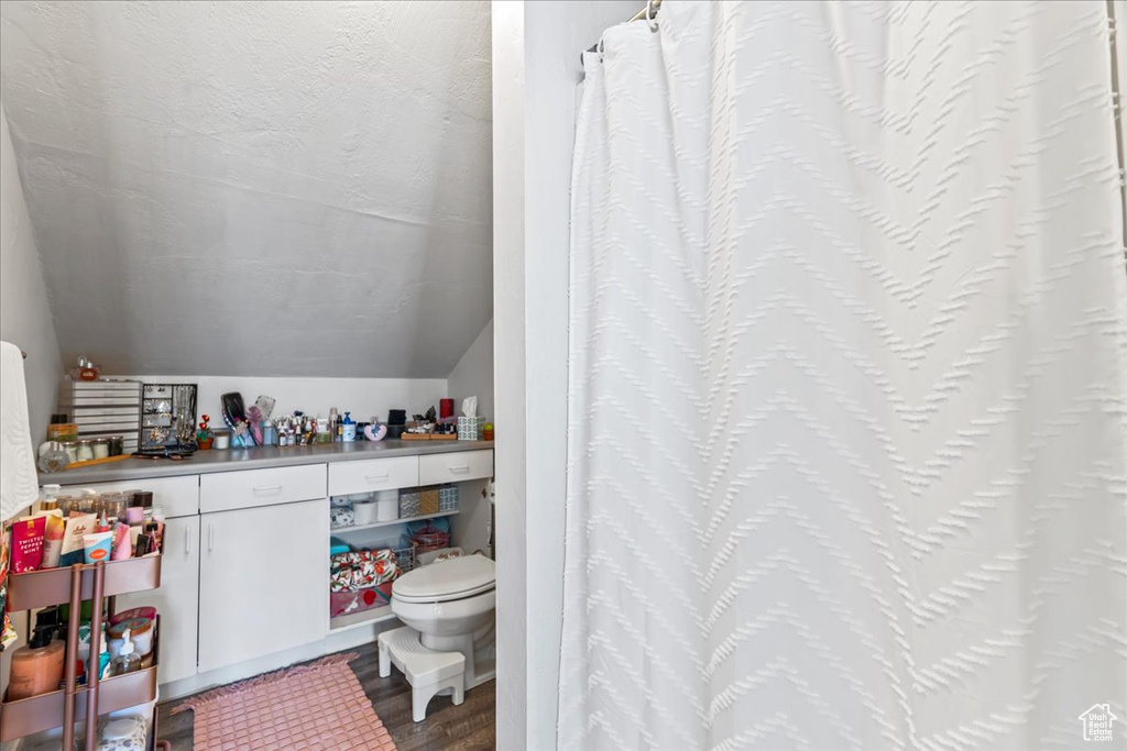 Bathroom featuring hardwood / wood-style flooring, toilet, vaulted ceiling, and a textured ceiling