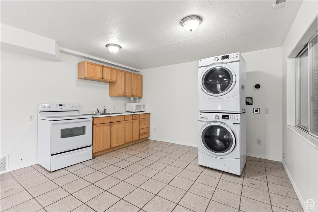 Interior space featuring light tile patterned flooring, stacked washing maching and dryer, sink, and a textured ceiling