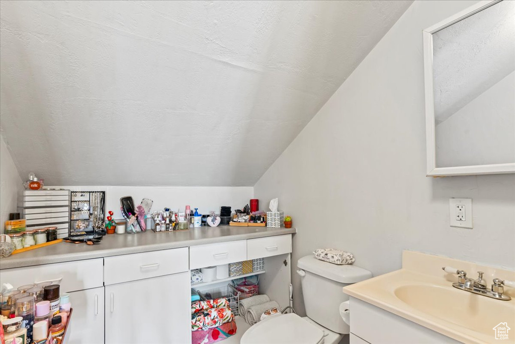 Bathroom with lofted ceiling, vanity, toilet, and a textured ceiling