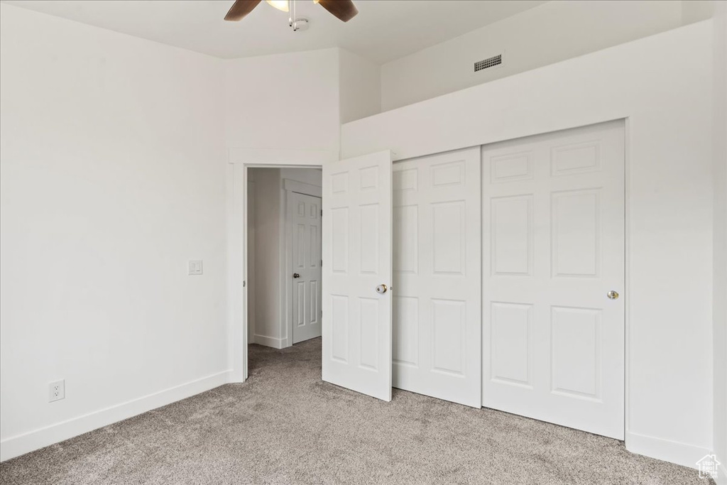Unfurnished bedroom with light colored carpet, ceiling fan, and a closet