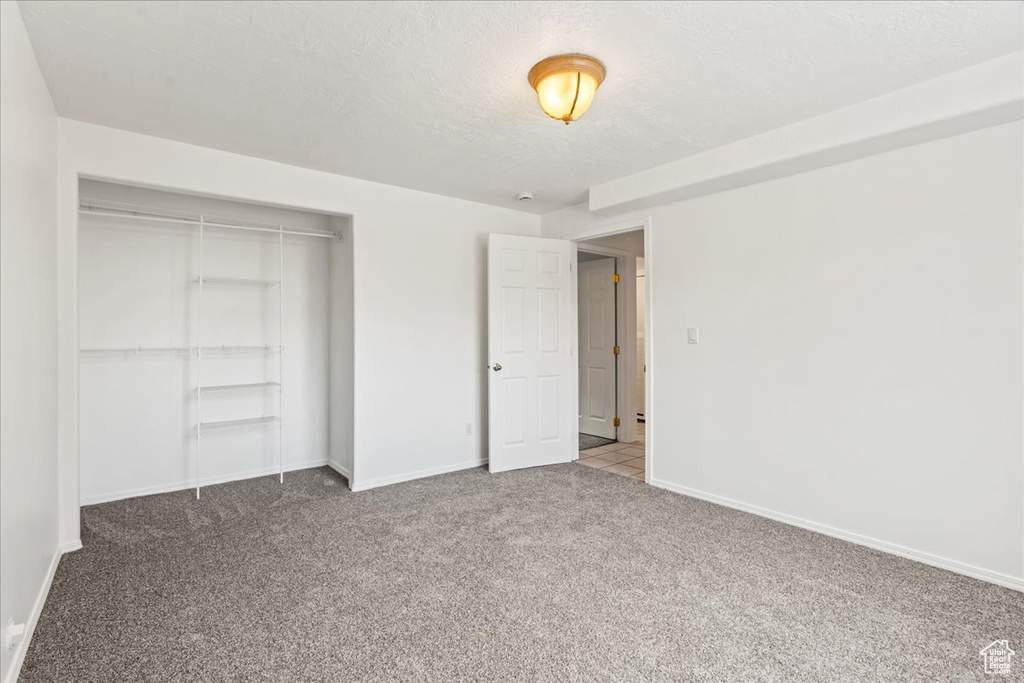 Unfurnished bedroom featuring carpet floors, a textured ceiling, and a closet