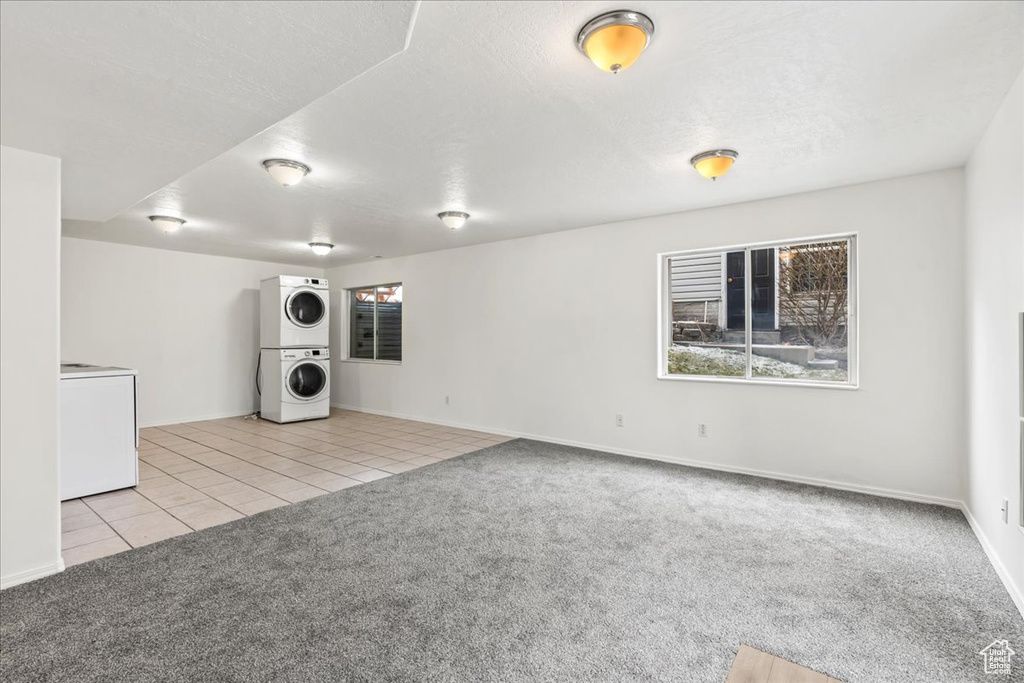 Empty room with light colored carpet, stacked washer / drying machine, and a textured ceiling