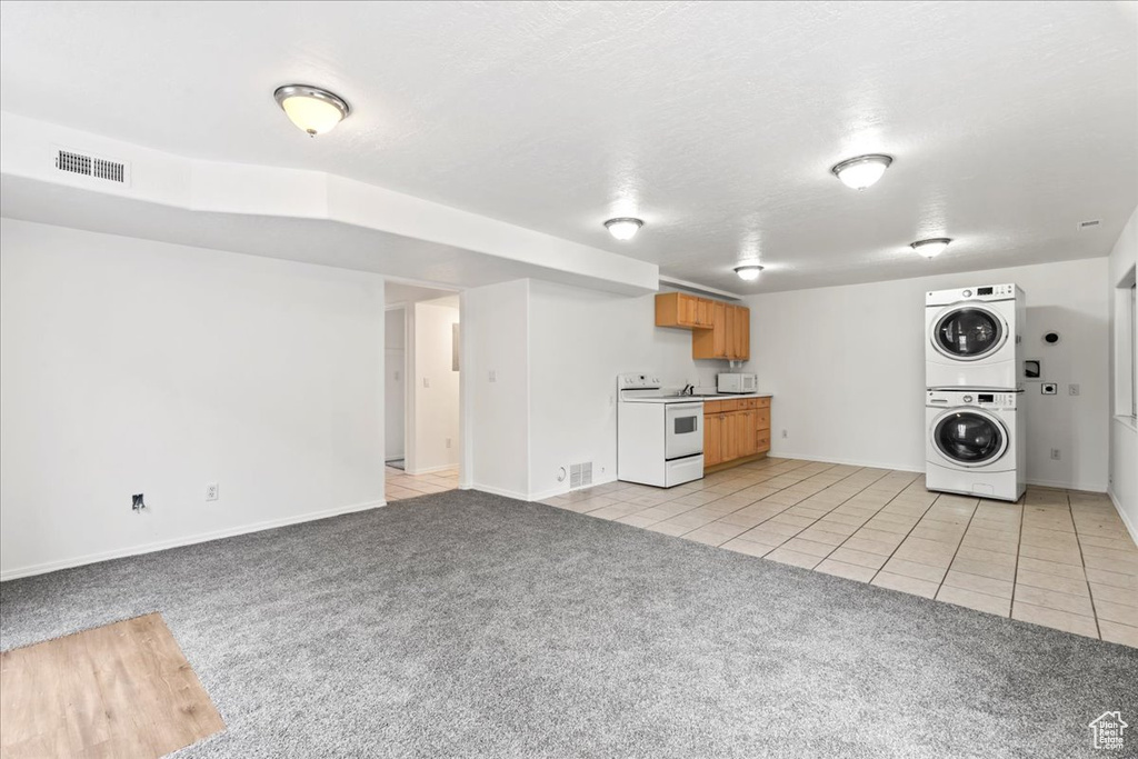 Kitchen with white appliances, light colored carpet, a textured ceiling, and stacked washing maching and dryer