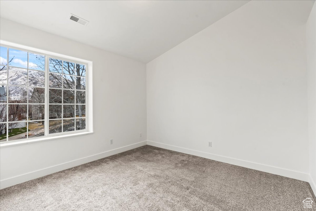 Carpeted spare room featuring vaulted ceiling