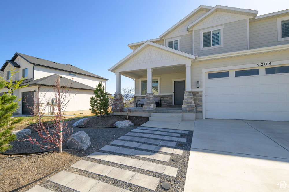 View of front of home featuring concrete driveway, stone siding, a garage, and covered porch