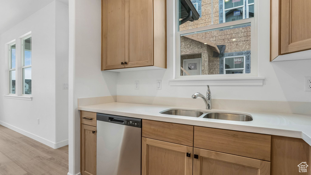 Kitchen featuring stainless steel dishwasher, a sink, light wood-style floors, light countertops, and baseboards