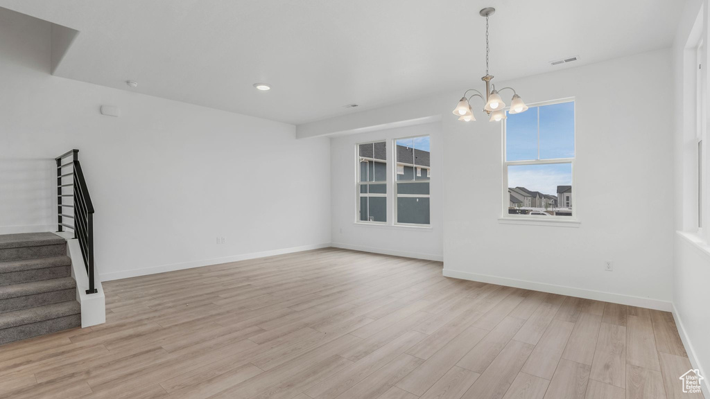 Unfurnished living room featuring stairs, light wood-style floors, a chandelier, and baseboards