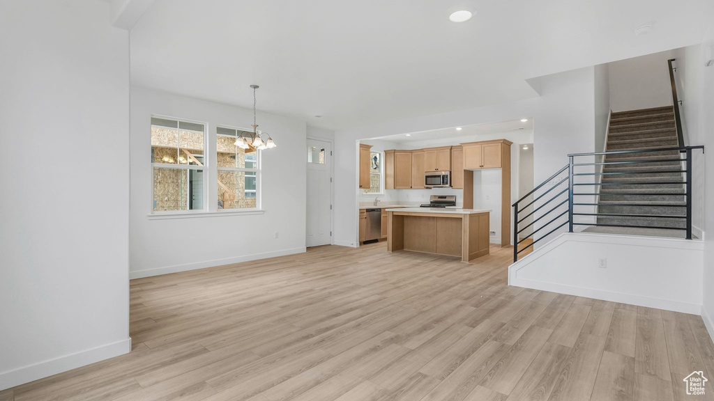 Unfurnished living room with a chandelier, stairs, light wood-style floors, baseboards, and recessed lighting