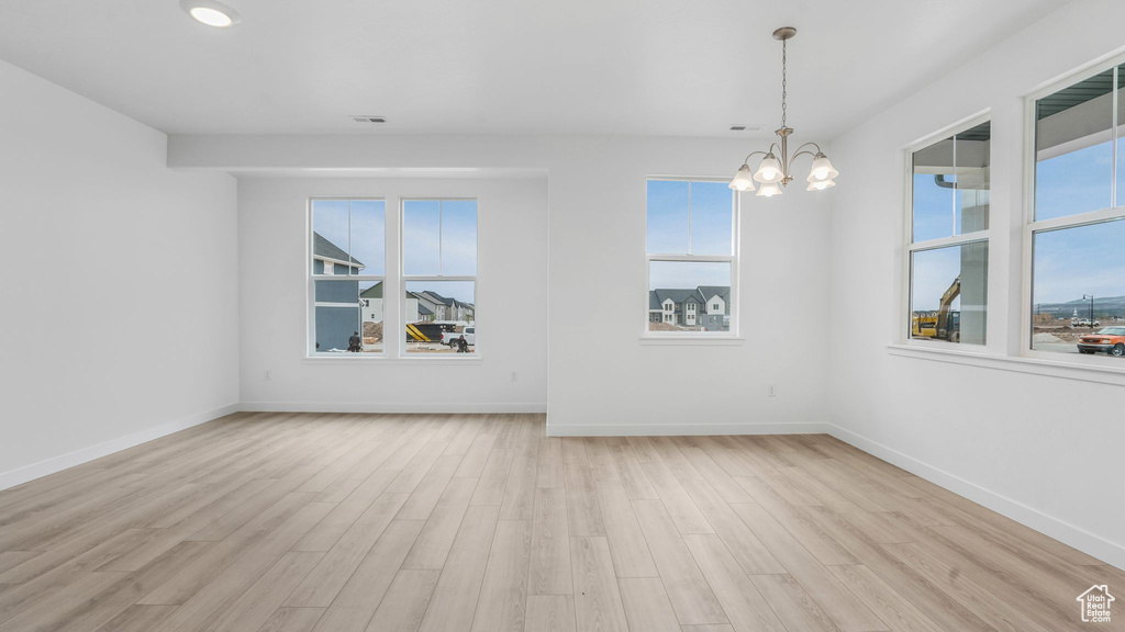 Empty room with healthy amount of natural light, wood finished floors, a chandelier, baseboards, and recessed lighting