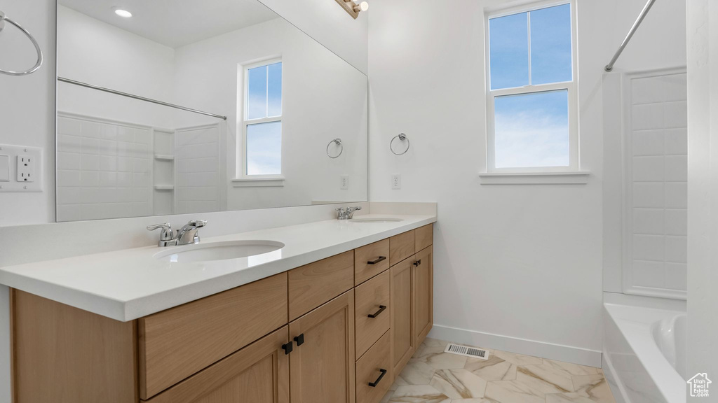 Bathroom with marble look tiles, baseboards, double vanity, and shower / bath combination