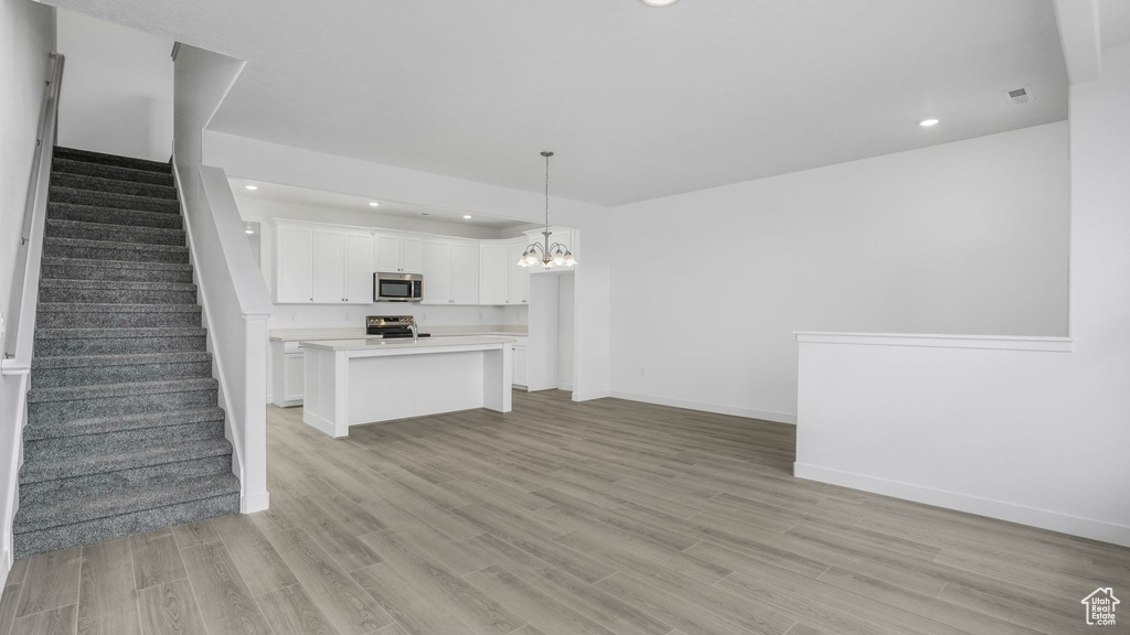 Unfurnished living room featuring stairs, a chandelier, recessed lighting, light wood-style floors, and baseboards